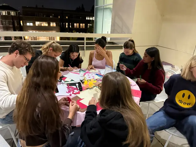 Students gathered around a table covered in craft supplies, decorating cards together.