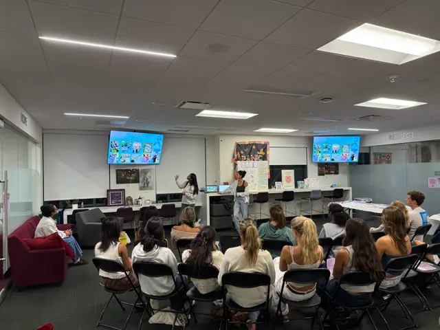 Students seated in rows watching a presenter at the front of a meeting room.