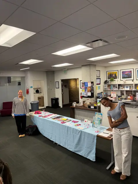 Two students staffing an indoor information table with a pale blue cloth and printed handouts.