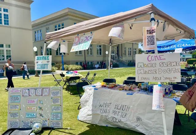 An outdoor tabling tent with hand-lettered posters asking passers-by which health issues matter to them.
