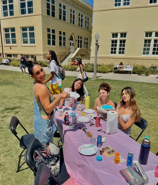 Students seated at a pink-clothed table on the lawn during an outdoor event.