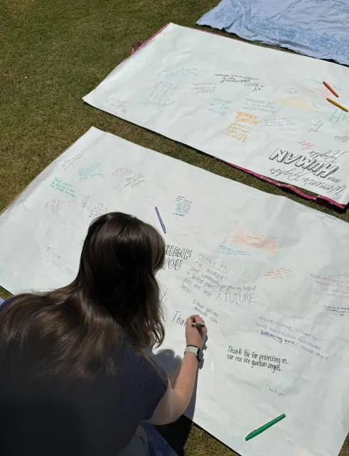 A student adding a handwritten message to large paper banners spread across the grass.