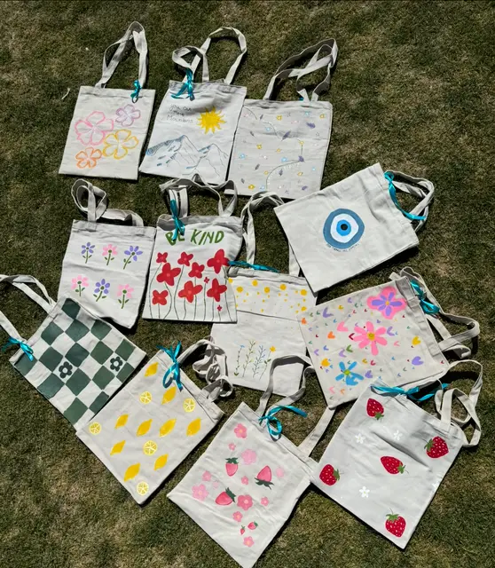 Finished hand-decorated tote bags laid out on the grass to dry.