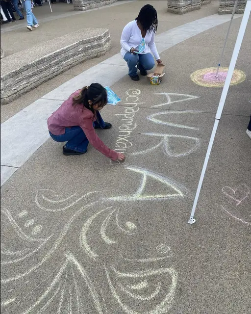 A student chalking the AURA name onto a campus walkway.