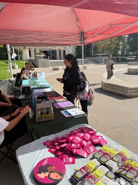 An outdoor table under a red canopy stocked with pink information packets.