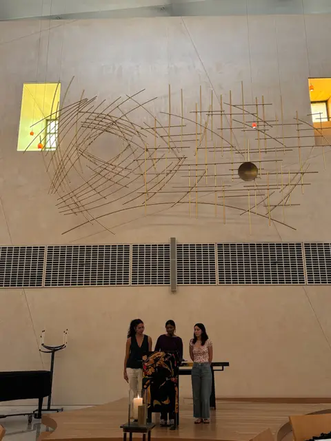 Three students standing together on stage in a campus auditorium.