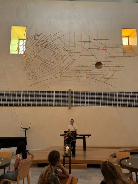 A student speaking from the stage at an event, with the audience seated in the foreground.