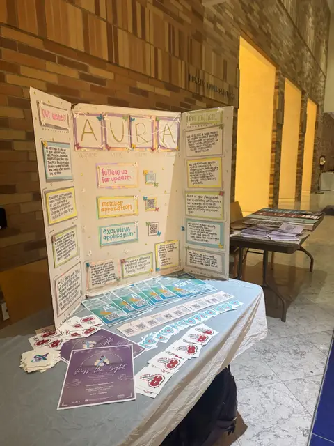 A trifold AURA display board set up on a table alongside printed handouts.
