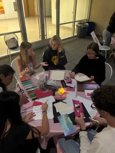 Students seated around tables working on a group craft activity.