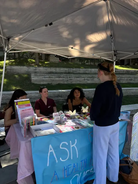 A student at the "Ask a health provider questions" table during an outdoor campus event.